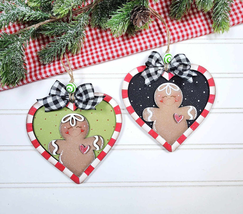 Heart-shaped gingerbread man ornaments with checkered ribbons on a white surface with Christmas decorations.