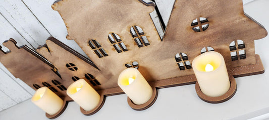 Wooden house-shaped candle holder with lit candles on a white surface