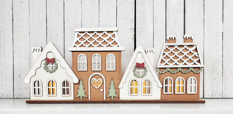 Set of four decorative gingerbread house-shaped candles on a wooden surface.