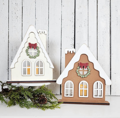 Two decorative house-shaped lanterns with wreaths and bows on a wooden background