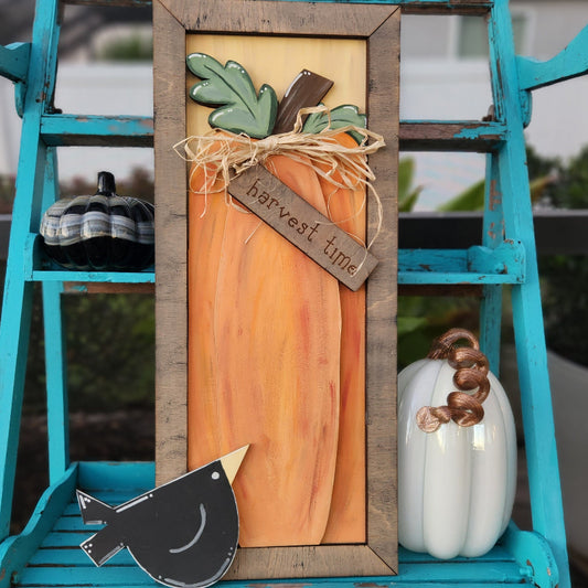 A framed 3D plank decoration featuring a harvest pumpkin and the text 'Harvest Time' displayed on a blue wooden surface with a bird and pumpkin.
