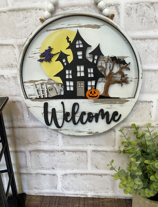 Haunted House interchangeable wooden Welcome sign insert featuring a black haunted house, yellow full moon, flying witch, graveyard, bats, spooky tree and orange jack-o'-lantern.