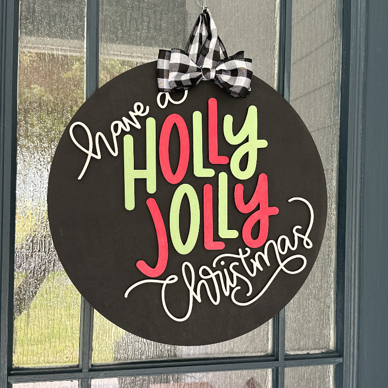 Decorative sign with 'Have a Holly Jolly Christmas' text on a black background, hanging on a door.