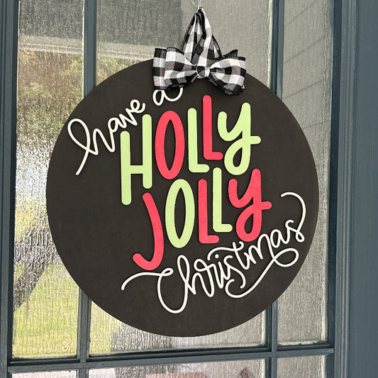 Decorative sign with 'Have a Holly Jolly Christmas' text on a black background, hanging on a door.