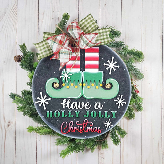Decorative Christmas sign with elf shoes, presents, and 'Holly Jolly Christmas' text on a wooden background.