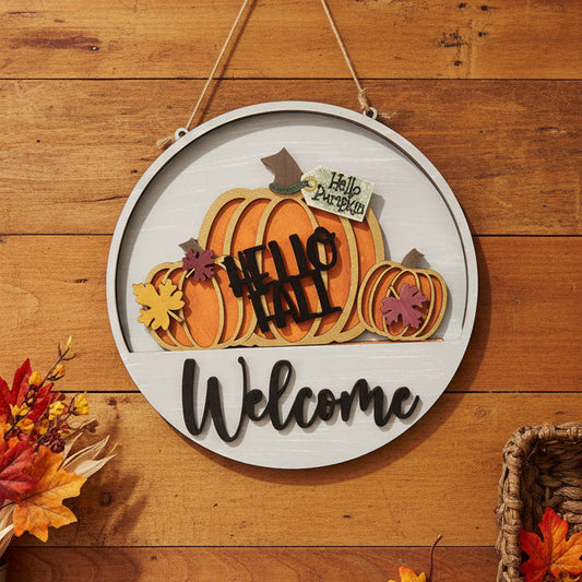 Round hanging wooden welcome sign with autumn pumpkins, fall leaves, and the words 'Hello Spring Back' and 'Welcome' on a white slatwall background.