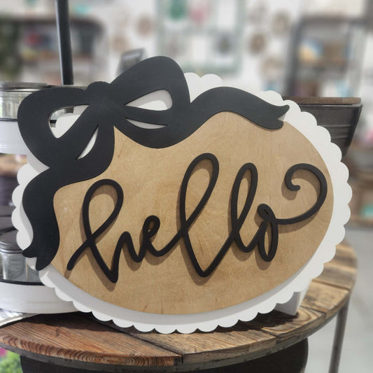 Wooden sign with 'hello' and a black bow on a wooden surface.