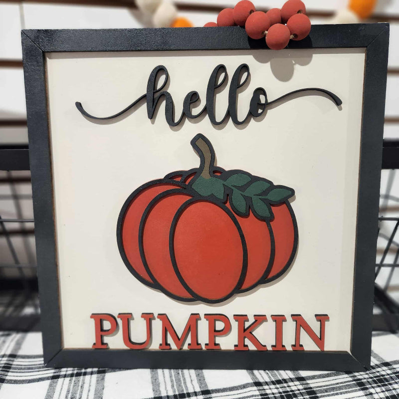 Decorative sign with a pumpkin and 'hello pumpkin' text on a plaid surface.