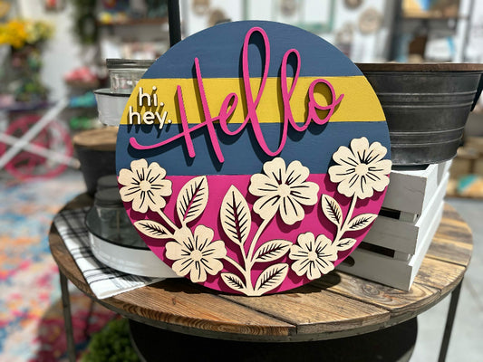 Decorative sign with floral designs and 'hello' text on a wooden surface.
