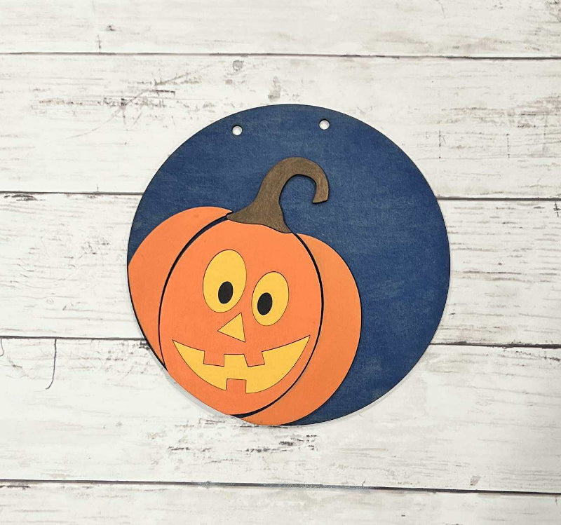 Pumpkin-shaped decoration with a jack-o'-lantern face on a blue background, placed on a wooden surface.