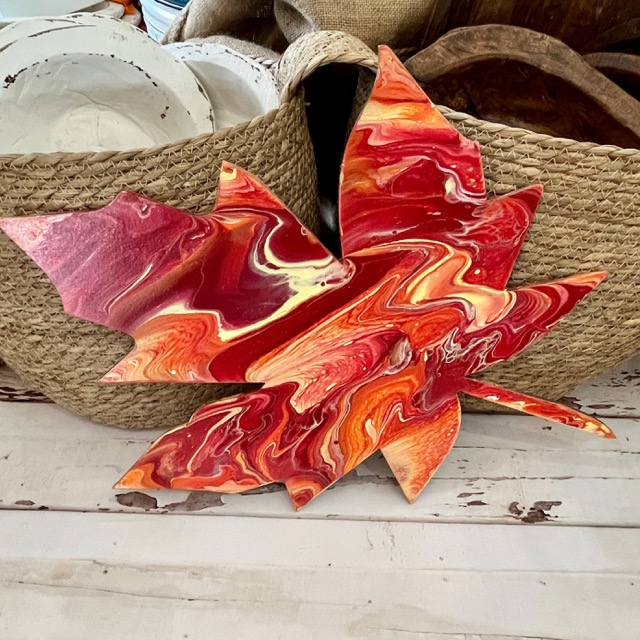 A piece of abstract pour art with red, orange, and white colors, displayed on a wooden surface.