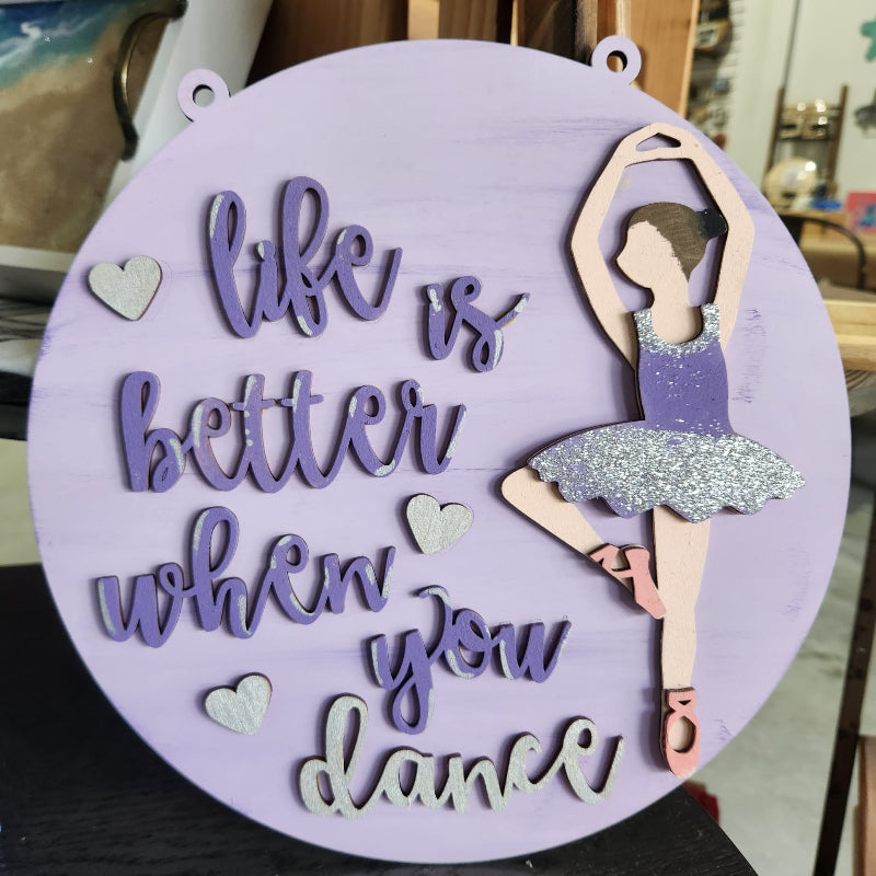 Decorative sign with a ballerina and 'life is better when you dance' text on a purple background.