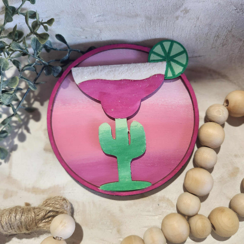 Decorative item with pink and green design on a textured surface with beads and plants.