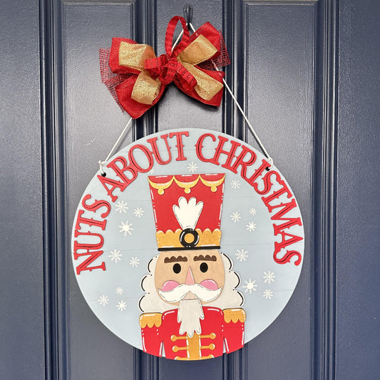 Nutcracker soldier on a blue round door hanger that says Nuts About Christmas 