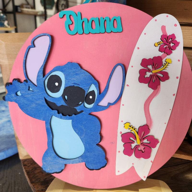 Decorative sign with a blue character, pink flowers, and 'Ohana' text on a pink background.
