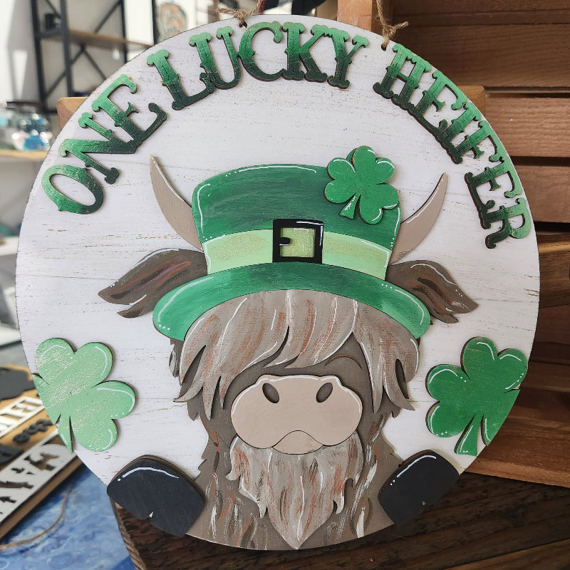 Decorative sign with a cow wearing a leprechaun hat and shamrocks, text 'ONE LUCKY HEIFER'.