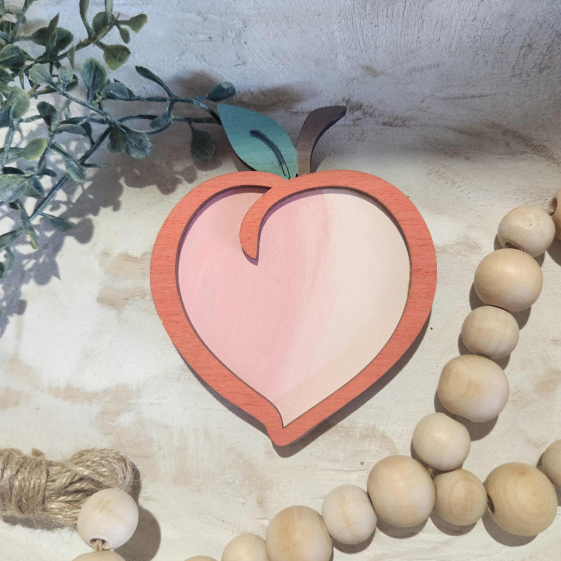 Decorative peach item on a textured surface with wooden beads and greenery.