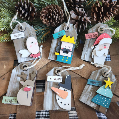 A collection of wooden gift tags with 3D ornaments including a bird, a crown, Santa Claus, a reindeer, a snowman, and a Christmas tree, all with festive messages.