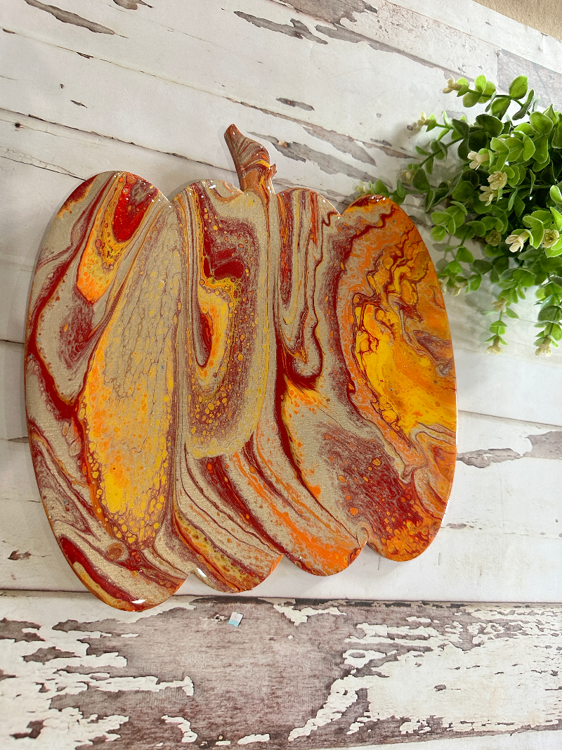 A vibrant pumpkin swirled in oranges and reds cut out of wood set on a wooden background