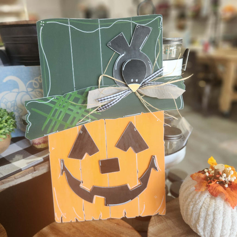 A handmade wooden Halloween decoration featuring a layered jack-o'-lantern and top hat design, styled on a wooden table with seasonal decor in a home setting.