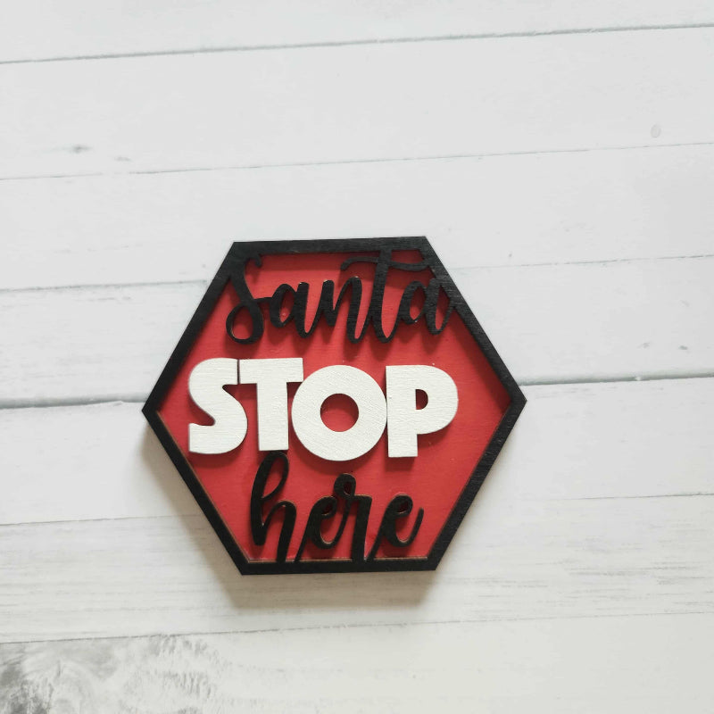 Hexagonal sign with 'Santa Stop Here' text on a white wooden surface