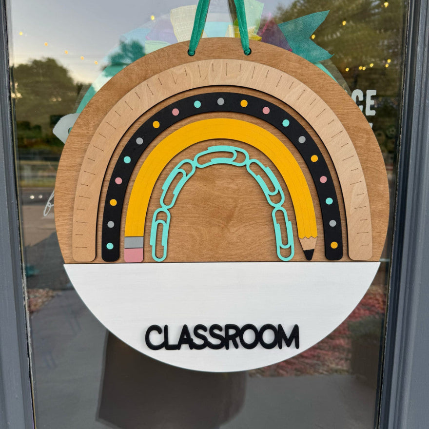 Decorative classroom sign with rainbow design and 'CLASSROOM' text on a glass door.