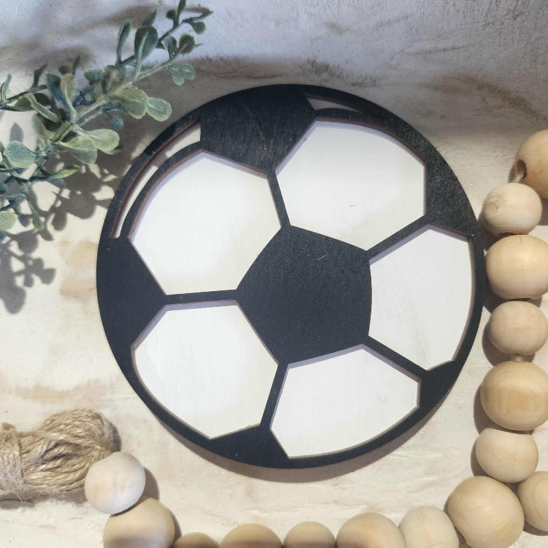Soccer ball-shaped object on a textured surface with wooden beads and greenery.