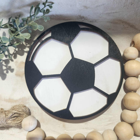 Soccer ball-shaped object on a textured surface with wooden beads and greenery.