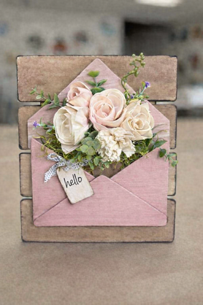 Decorative pink envelope with flowers and a 'hello' tag on a wooden stand.