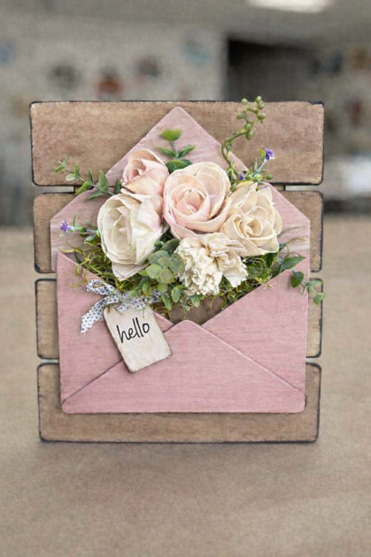 Decorative pink envelope with flowers and a 'hello' tag on a wooden stand.