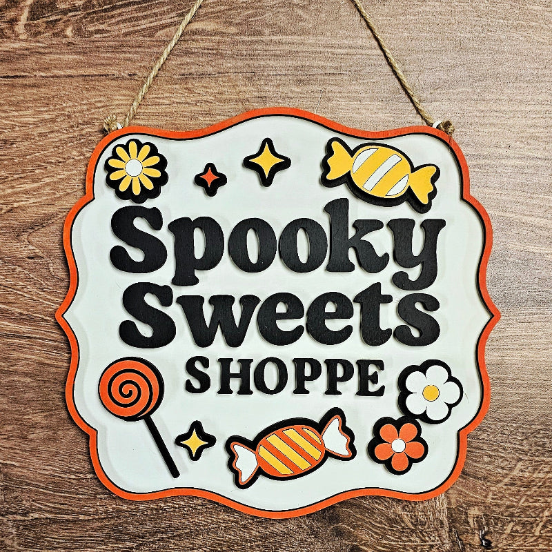 Decorative sign with 'Spooky Sweets Shoppe' text and candy-themed graphics on a wooden background.