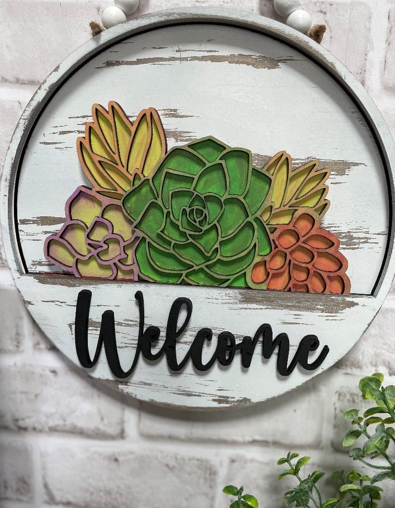 Succulent Garden interchangeable wooden Welcome sign insert featuring layered green, purple, yellow and coral succulents in a rustic round door hanger.