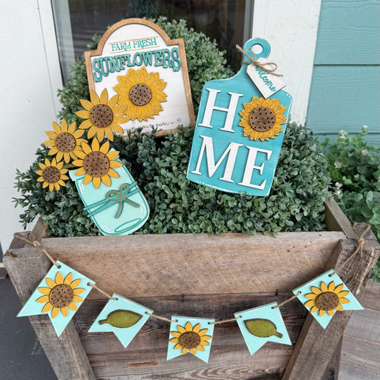 Decorative sunflower-themed signs and bunting in a wooden planter with greenery.