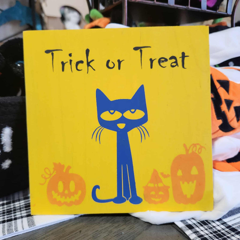 Yellow book with a blue cat illustration and 'Trick or Treat' text, surrounded by Halloween-themed items.