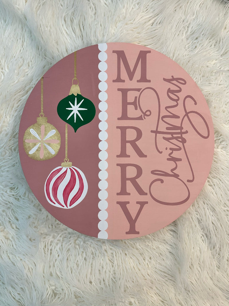 Round decorative sign with Christmas ornaments and 'Merry Christmas' text on a fluffy white surface.