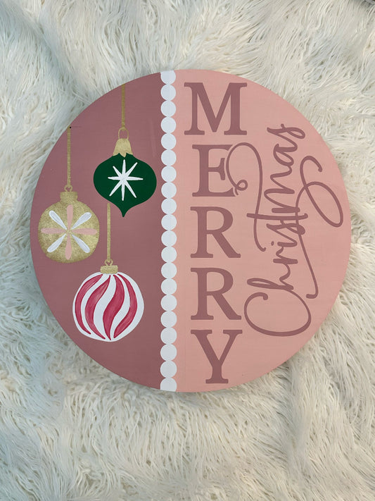 Round decorative sign with Christmas ornaments and 'Merry Christmas' text on a fluffy white surface.