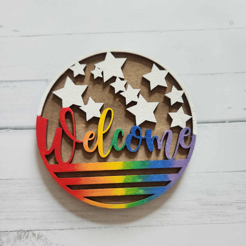 Wooden wall decor with 'Welcome' in rainbow colors and white stars on a light wooden background