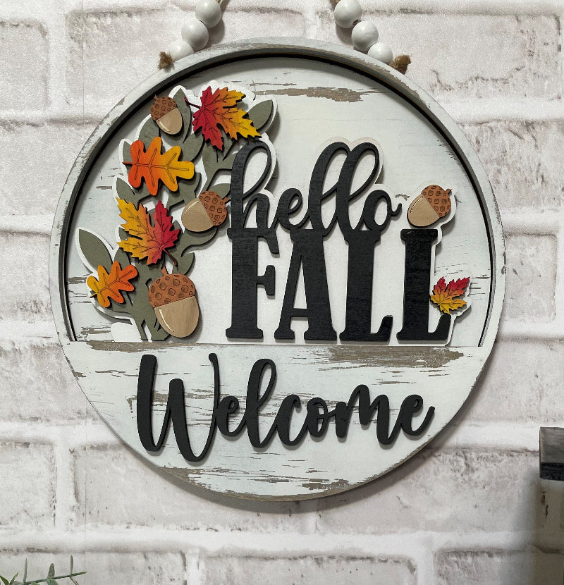 Alt text: Hello Fall interchangeable wooden Welcome sign insert with layered orange, red and yellow autumn leaves, acorns and black lettering.