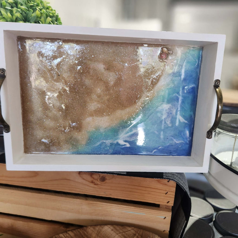 Epoxy filled tray ith a beach scene inside, placed on a wooden surface.
