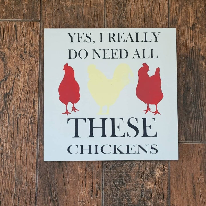 A square-shaped wooden plaque with a white background, featuring red silhouettes of chickens and the text 'YES, I REALLY DO NEED ALL THESE CHICKENS'.